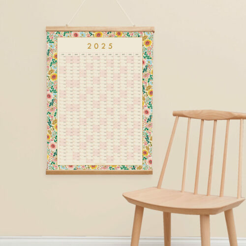 a styled photo of a 2025 floral wall planner with a light wooden chair and neutral wall colour