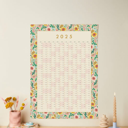 a styled shot of a floral 2025 wall planner over a shelf with other matching stationery items on show on a neutral wall background