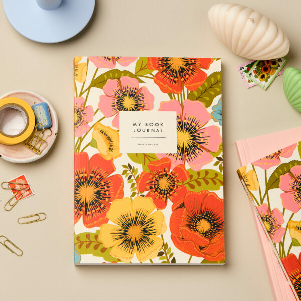 Bloom Lay-Flat Reading Journal – Hand-Drawn Flower Design cover styled as a flat lay with other notebooks, a candle and stationery