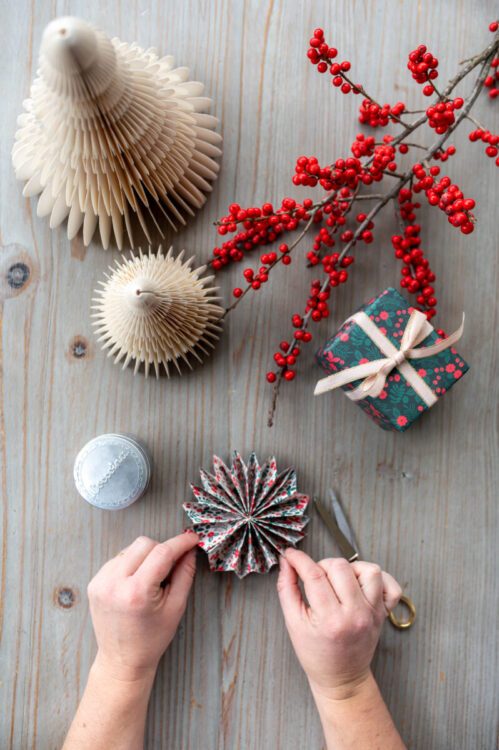 Beautiful handmade paper star garland Christmas decoration DIY made with Lucy says I do double sided Christmas wrapping paper styled with Christmas berries and a little wrapped gift tied with ribbon, and paper trees plus glue pot