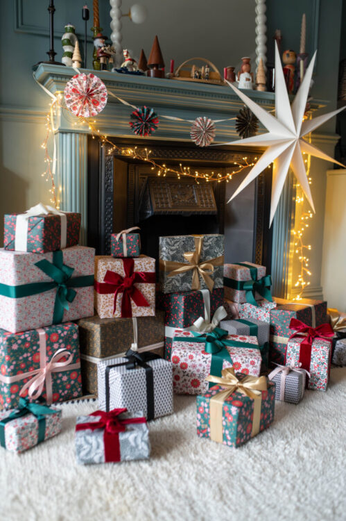 Beautiful fireplace in living room decorated for Christmas with fairy lights, a large paper star, a DIY star garland, wrapped gifts using Lucy says I do double sided gift wrap. Room is painted in Farrow and Ball Oval Blue