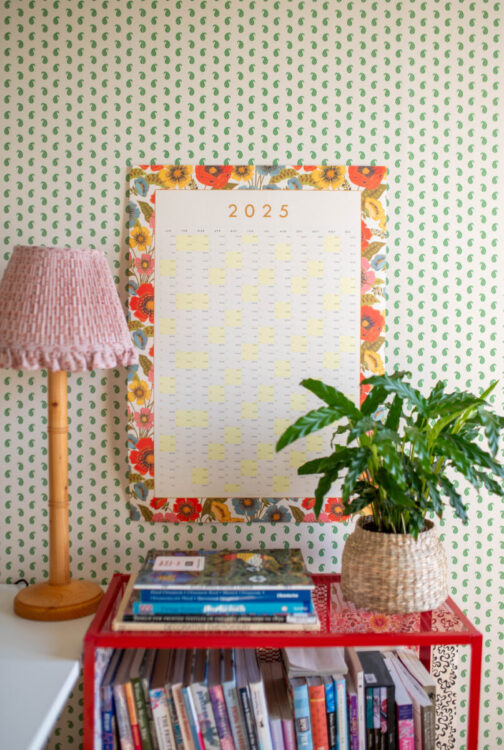 Large floral bright Bloom 2025 wall planner styled in front of pattern Morris wallpaper